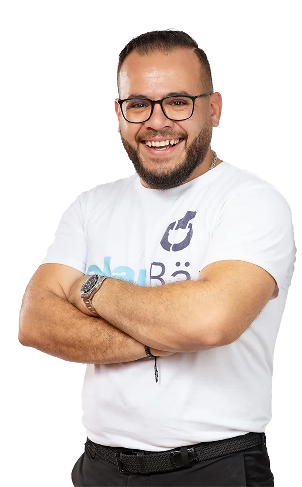 Fröhlicher Mann mit Brille und Bart, trägt weißes T-Shirt mit Logo, verschränkt die Arme, professioneller Auftritt.